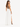 A woman stands in profile wearing a fitted brown top and a flowing white skirt with a side slit.