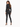 A woman with long hair wears a cropped black jacket and fitted black pants, paired with high-heeled sandals.