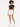 A model poses in a black cropped top and white high-waisted shorts, paired with white sneakers.
