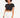 A young woman with curly hair wears a fitted black top and white high-waisted shorts, posing confidently.