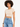 A young woman with curly hair wears a fitted beige crop top paired with high-waisted distressed blue jeans.