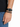 A close-up of a hand wearing a black leather watch and a beaded bracelet with alternating black and gray beads.