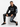 A man sits on a white cube wearing black sweatpants with graphic prints and a matching hoodie, paired with black snea...