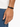 A close-up of a hand wearing a minimalist black bracelet with a sleek clasp, set against a light background.
