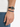 A close-up of a hand wearing a colorful beaded bracelet alongside a black leather watch.