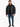 A man stands wearing a black puffer coat, black shirt, distressed jeans, and sneakers against a white background.