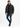 A man wearing a black puffer coat, black shirt, distressed jeans, and sneakers poses against a white background.