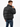 A man wearing a black puffer coat with a high collar, facing away and adjusting the zipper.