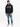 A man stands wearing a black hoodie with blue accents, paired with light blue jeans and stylish sneakers.