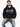 A man sits on a stool wearing a black hoodie with graphic text and blue accents, paired with blue jeans.