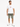 A man stands wearing a white graphic t-shirt and olive green distressed shorts, paired with white sneakers.