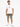 A man stands wearing a white graphic t-shirt and olive green distressed shorts, paired with white sneakers.