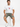 A man sits on a white pedestal wearing a white graphic t-shirt and olive green shorts, paired with white sneakers.