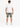 A man stands with his back to the camera, wearing a white t-shirt and olive green shorts, paired with white sneakers.