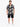 A man stands wearing a short-sleeve button shirt with a black and white graphic print, paired with black shorts.