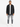 A man stands confidently wearing a black button-up top over a white t-shirt, paired with distressed gray jeans and wh...