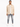 A man stands confidently in a light beige button-up top, paired with distressed gray jeans and white sneakers.
