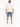 A man stands with his back to the camera, wearing denim shorts and a loose-fitting white t-shirt.