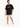 A man stands wearing a black oversized t-shirt and light gray denim shorts with rolled cuffs, paired with white sneak...