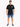 A man stands wearing rolled denim shorts, a black t-shirt with graphic text, and stylish sneakers.