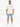 A person stands wearing a loose-fitting beige t-shirt and light blue denim shorts, paired with white sneakers.