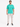 A man stands wearing a turquoise t-shirt with white text, paired with light cargo pants and black sneakers.