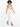 A model with curly hair wears a fitted beige top and white tailored pants, paired with black high-heeled sandals.