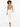 A model with curly hair wears a tan sleeveless top paired with white tailored pants and black strappy heels.