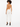 A woman with curly hair wears a tan bodysuit with a stylish back design, paired with white pants and black heels.