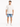 A man stands wearing a loose-fitting white t-shirt and distressed denim shorts, paired with white sneakers.