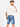 A man wearing a loose-fitting cream t-shirt and blue denim shorts, looking back over his shoulder.