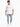 A man stands wearing a loose white t-shirt and distressed light blue jeans with multiple rips, paired with white snea...