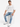 A man sits on a white pedestal wearing distressed light blue jeans, a loose white t-shirt, and white sneakers.