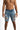 A man wearing distressed denim shorts with multiple rips and a light wash, standing against a white background.