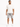 A man stands wearing a loose-fitting white t-shirt and distressed gray denim shorts, paired with white sneakers.