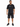 A man stands wearing a black graphic t-shirt and distressed black shorts, paired with black sneakers.
