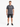 A man stands wearing a gray t-shirt and black denim shorts, paired with stylish black sneakers.