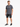 A man stands wearing a gray t-shirt with a graphic design, paired with distressed black shorts and stylish sneakers.