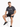 A man sits on a white stool wearing a dark gray t-shirt and black shorts, paired with stylish sneakers.