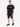 A man stands confidently in a black t-shirt paired with distressed denim shorts and stylish sneakers.