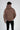 A person wearing a brown hoodie with a large hood, facing away, paired with black jeans.