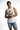 A young man in a sleeveless white shirt and distressed denim shorts poses with his hands clasped.