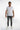 A man stands confidently in a fitted white t-shirt and gray jeans, complemented by white sneakers.