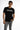A young man poses in a black short-sleeve shirt featuring a graphic text design, paired with distressed gray jeans.