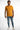 A man stands confidently in a fitted orange shirt paired with distressed blue jeans and white sneakers.
