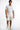 A man wearing a fitted white t-shirt and distressed white shorts with colorful paint splatters, paired with white sne...
