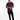 A man stands confidently in a purple short-sleeve shirt and black jeans, wearing white sneakers.