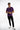 A man stands confidently in a purple short-sleeve shirt and black jeans, wearing white sneakers.
