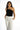 A model poses in a stylish black one-shoulder top paired with tailored white trousers.