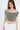 A model poses in a soft, off-the-shoulder, cropped top in a muted green shade, paired with a white skirt.